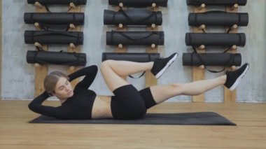 Genç fitness kadını aerobik yapıyor. Beden eğitimi yapıyor. Sırt üstü paspasın üzerinde yatıyor. Beden eğitiminde kol ve bacakların karın kasları üzerinde pilates çalışması yapar