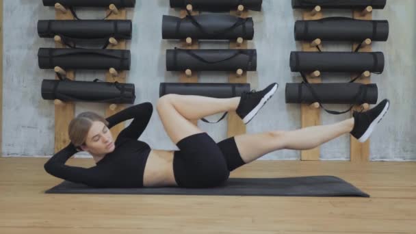若いフィットネス女性は マットの上の床の上に横たわってエアロビクスの物理的な演習を行う パフォーマンスジムで腕や足の腹部の筋肉トレーニングのピラティスのトレーニング — ストック動画