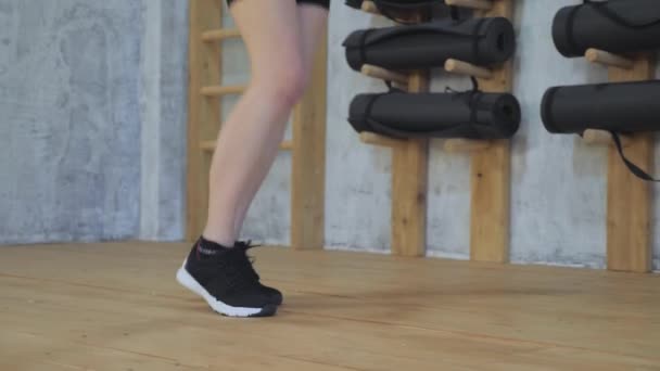 女子脚踏运动鞋跳绳在室内健身房的慢动作射击 运动鞋跳绳女足的特写穿着运动服 黑色上衣和运动服的女足在健身房里 — 图库视频影像