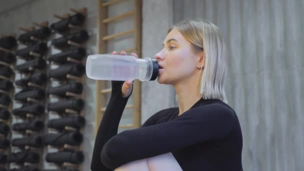 健身女孩在家里或健身房运动暂停时喝运动瓶子里的水 活动妇女在训练后休息时从水瓶中喝水的闭合背光肖像 — 图库视频影像