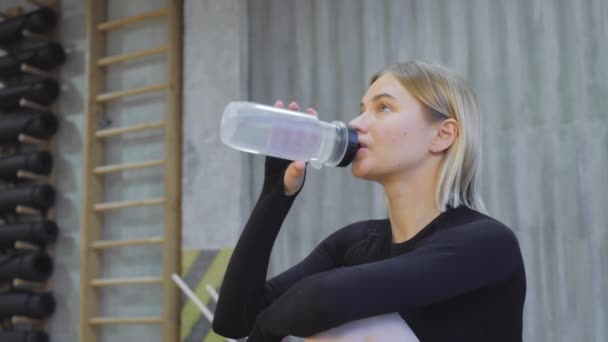 運動の後にボトルから水を飲む若いアスレチックブロンドの女性ブラックトップとライトジムのレギンスに身を包んだ — ストック動画