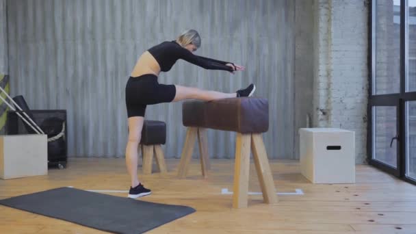 身材苗条的年轻女子在健身馆的体操酒吧里锻炼 伸展运动 定期运动 运动女性穿着黑色上衣和腿在明亮的健身房做体操前伸展运动 — 图库视频影像