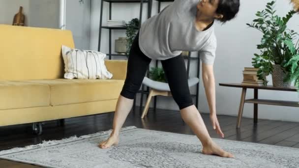 若い女性が瞑想運動ストレッチスポーツヨガ 服黒レギンスとトップ 自宅で明るい部屋 — ストック動画