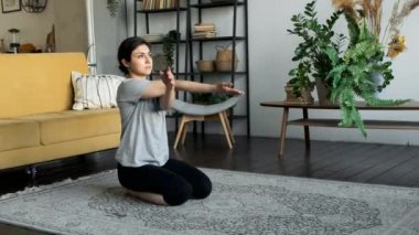 Hintli bir kadın yerde oturur ve yoga egzersizi için hazırlanır, ısınır ve kaslarını gerer, kollarını bükme egzersizi yapar. Evinde, rahat bir odada.