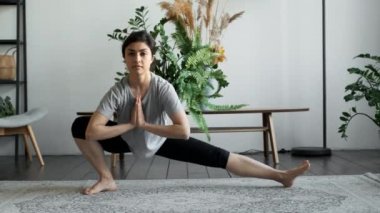Bir Hintli Kadın Yoga egzersizi için yerde oturur ve hazırlanır, ısınma egzersizleri ve kas germe egzersizleri yapar, sağa ve sola çömelme egzersizleri yapar. Evinde, rahat bir odada.
