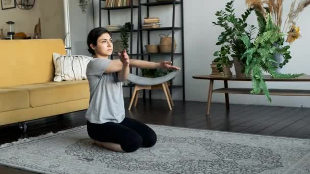 一位印度妇女坐在地板上 准备进行瑜伽锻炼 做热身和肌肉伸展运动 做扭臂运动 位于家中一个舒适的房间里 — 图库视频影像
