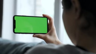 A Woman's Hand Holds A Smartphone With A Green Screen For Chromakey, Watches Social Networks, Movies, Videos, Lies on The Sofa in A Cozy Room
