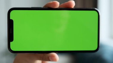 Close-Up Of A Woman's Hand Holding Horizontally A Smartphone with A Green Screen, Chromakey For Use