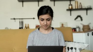 Genç Hintli kadın, Düşüncelere dalmış, bir dizüstü bilgisayarda çalışıyor, çevrimiçi eğitim ya da iş yapıyor, evinde rahat bir odada çalışıyor.