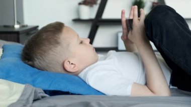 Çocuk kanepede akıllı telefondan oyun oynuyor. Anaokulu öğrencisi cep telefonu çalıyor. Çocuk oyun oynamak için telefonu kullanıyor. Evde video oyunu oynayan çocuk