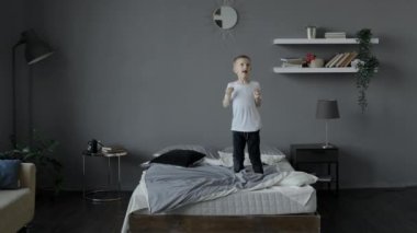Küçük bir çocuk güler ve sabah parlak bir odada yatağa atlar.