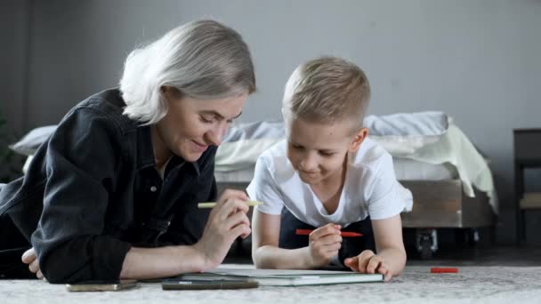 一个年轻的母亲和一个男孩躺在地板上 手握纸笔 一边读书 一边说话 一边玩乐 — 图库视频影像
