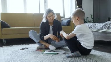 Genç bir anne ve bir bebek yerde oturuyor, anne çocuğa resim çizmeyi öğretiyor, çocuk kağıda keçeli kalemlerle resim çiziyor, eğitimle, konuşmayla ve eğlenmekle meşguller.