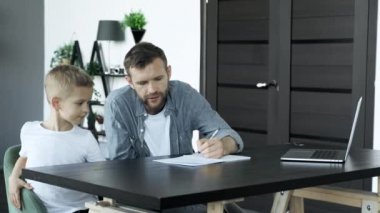 Supporting Son In His Studying. Side View Of Cheerful Young Father Helping His Son To Do Homework