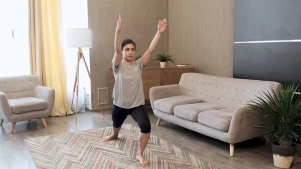 一位年轻的印度妇女正在做瑜伽 她站在一条腿上做着平衡运动 在一个明亮的房间里做身体伸展运动 — 图库视频影像