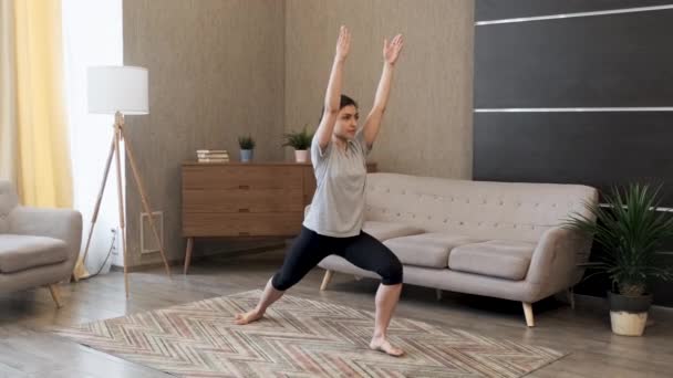 一个年轻女人做瑜伽 做运动保持平衡 穿运动服 呆在家里一间明亮的房间里 — 图库视频影像