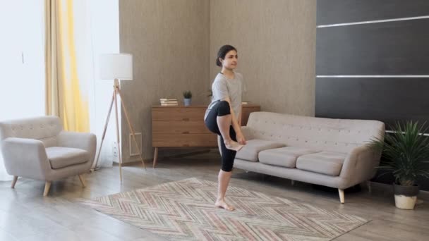 一个年轻的印度女人正在做瑜伽 用一条腿做运动来保持平衡 位于家中一间明亮的房间 — 图库视频影像