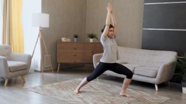Genç Asyalı kadın gülümseyerek evde yoga egzersizleri yapıyor, vücut sağlığı için kaslarını çalıştırıyor.