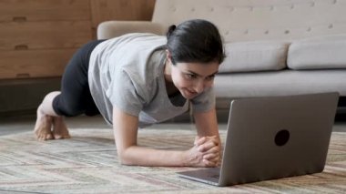 Genç ve çekici bir kadın evde spor yapıyor ve dizüstü bilgisayardan spor dersleri izliyor.