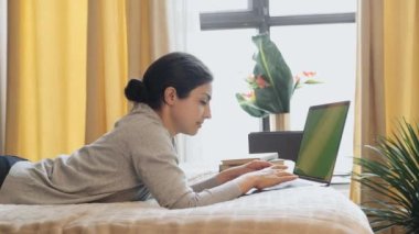 Yeşil Ekran Mock Up Girl kanepede oturuyor ve rahat bir akşam odasında dizüstü bilgisayardan sürekli izliyor.