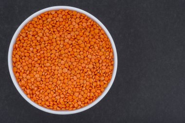 Beyaz cam kasede kırmızı mercimek. Koyu gri arkaplanda kırmızı mercimek resmi. İzole edilmiş yakın çekim fotoğrafı