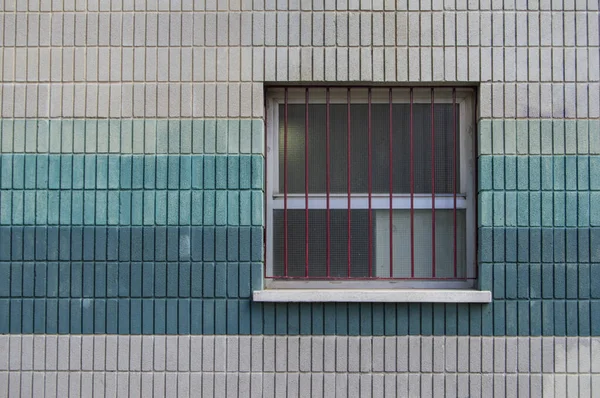 square window with grill on a brick wall painted teal