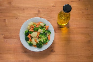 Karnabaharlı beyaz tabak, brokoli ve havuç ve bir şişe yağ, ahşap arka planda izole edilmiş.