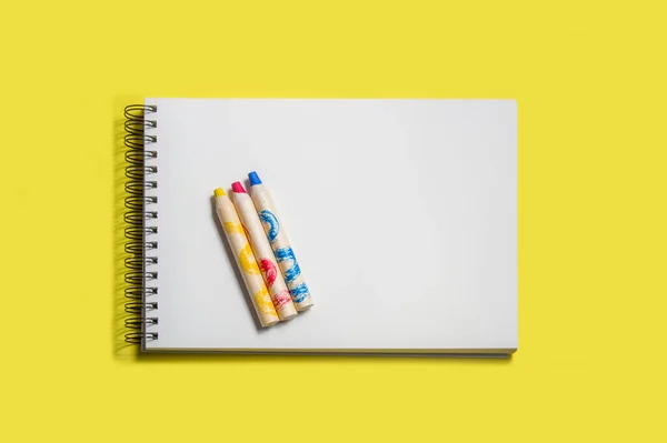 sketch pad with white sheets and three wooden pencils in yellow, red and blue colors, isolated on yellow background