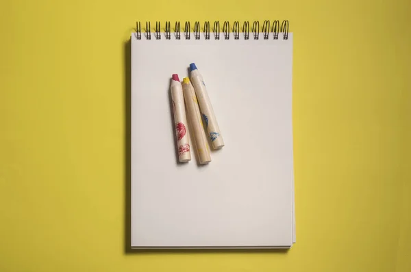 sketch pad with three red yellow and blue colored pencils, isolated on yellow background