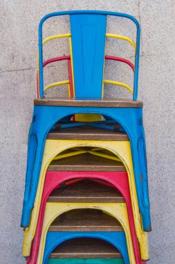 Sokakta duvarın yanına dizilmiş renkli metal sandalyeler.