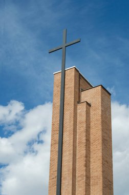 Demir haçlı modern tuğla kule, gökyüzü arka planında kesilmiş.