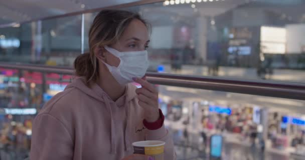 A young woman wearing a medical face mask and drinking coffee — стоковое видео