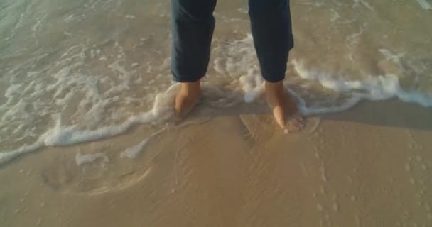 Çıplak ayaklı adam sahilde duruyor ve deniz dalgaları ayaklarını yıkıyor. — Stok video
