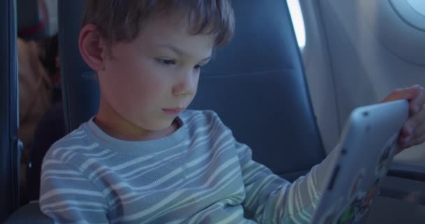 Boy olha para tablet com adesivos e tipos no avião — Vídeo de Stock
