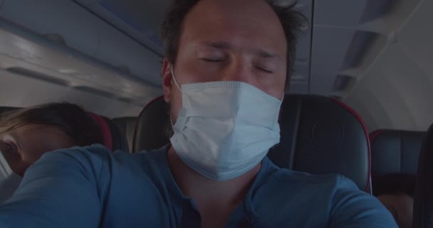 Спящий человек в маске просыпается и смотрит в окно самолета — стоковое видео
