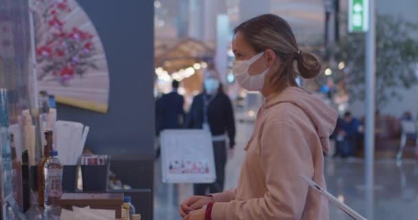 Mulher com máscara e mochila espera por ordem no bar de sushi — Vídeo de Stock
