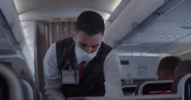 Наставник у формі й маска дає їжу пасажирам у літаку. — стокове відео