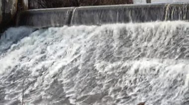 Köpüklü suyun dinamik görüntüsü yapay olarak oluşturulmuş bir nehir barajının üzerinde hızla akıyor ve kışın derinliklerinde canlı bir şelale oluşturuyor. Akış, doğanın güçlü bir görüntüsünü yaratır..