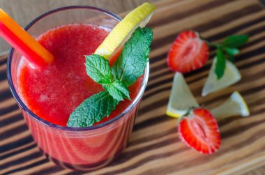 Limonlu çilekli smoothie, ahşap masada nane ve pipet. 