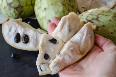 Siyah taştan bir masanın üzerinde kadının elinde dilimlenmiş Cherimoya.