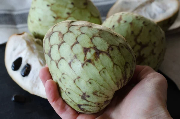 Elde Cherimoya, siyah bir taş masanın üzerinde başka bir Cherimoyas ile. 