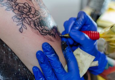 Bir kadının üst kolunda çiçek dövmesi yapma süreci. Yakın plan.,