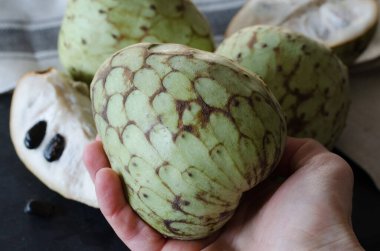 Siyah taş bir masa arkasında, bir kadının elinde dilimlenmiş Cherimoya.