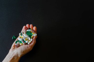 Bir sürü ilaç, hap, tablet, kapsüller, siyah mat arka planında kadın eli. Seçici odaklı makro fotoğraf. Tıbbi eczane geçmişi. Uzayı kopyala Yatay çerçeve