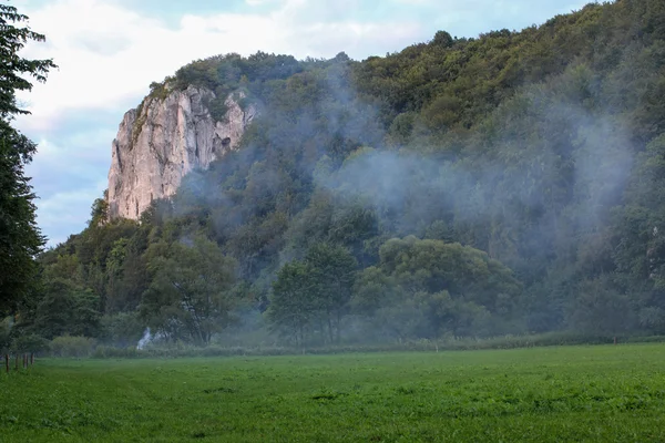 Humo de un fuego debajo de una montaña de piedra caliza al atardecer —  Fotos de Stock