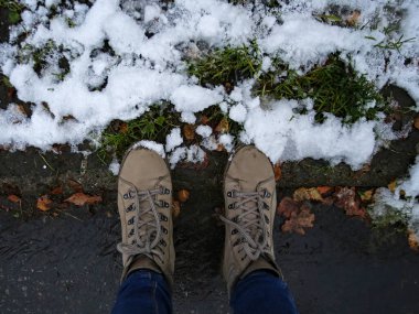 Sonbahar yaprakları karla kaplı bir sokakta duran botlar.