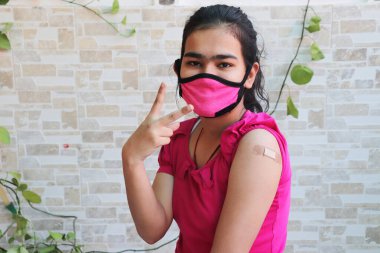 Hintli kız Covid-19 'un yeni türü sırasında aşı olduktan sonra zafer işareti yaptı, koluna koronavirüs aşısı uygulanan maskeli genç bir kadın. bağışıklık programı.