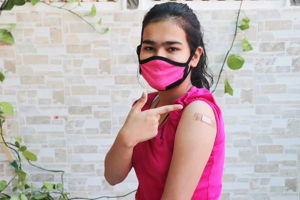 Hintli kız yeni covid-19 aşısı sırasında uygulanan bandajı gösteriyor, maske takan genç kız koluna koronavirüs aşısı yaptırmış. bağışıklık programı. Sars-cov-2