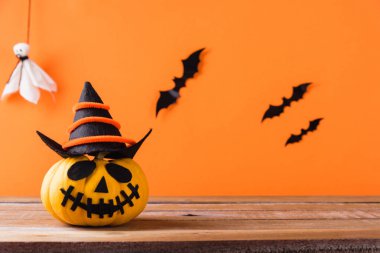 Komik Cadılar Bayramı dekorasyon partisi, şirin balkabağı hayaleti hayalet kabak fener maskesi şapka, siyah örümcek ve yarasalar ahşap masada, stüdyo çekimi turuncu arka planda, mutlu bayramlar konsepti