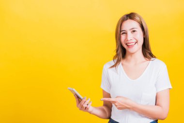 Asya Tayland portresi mutlu genç kadın gülümsüyor. Tişört giyiyor. Akıllı telefon ekranını işaret ediyor.